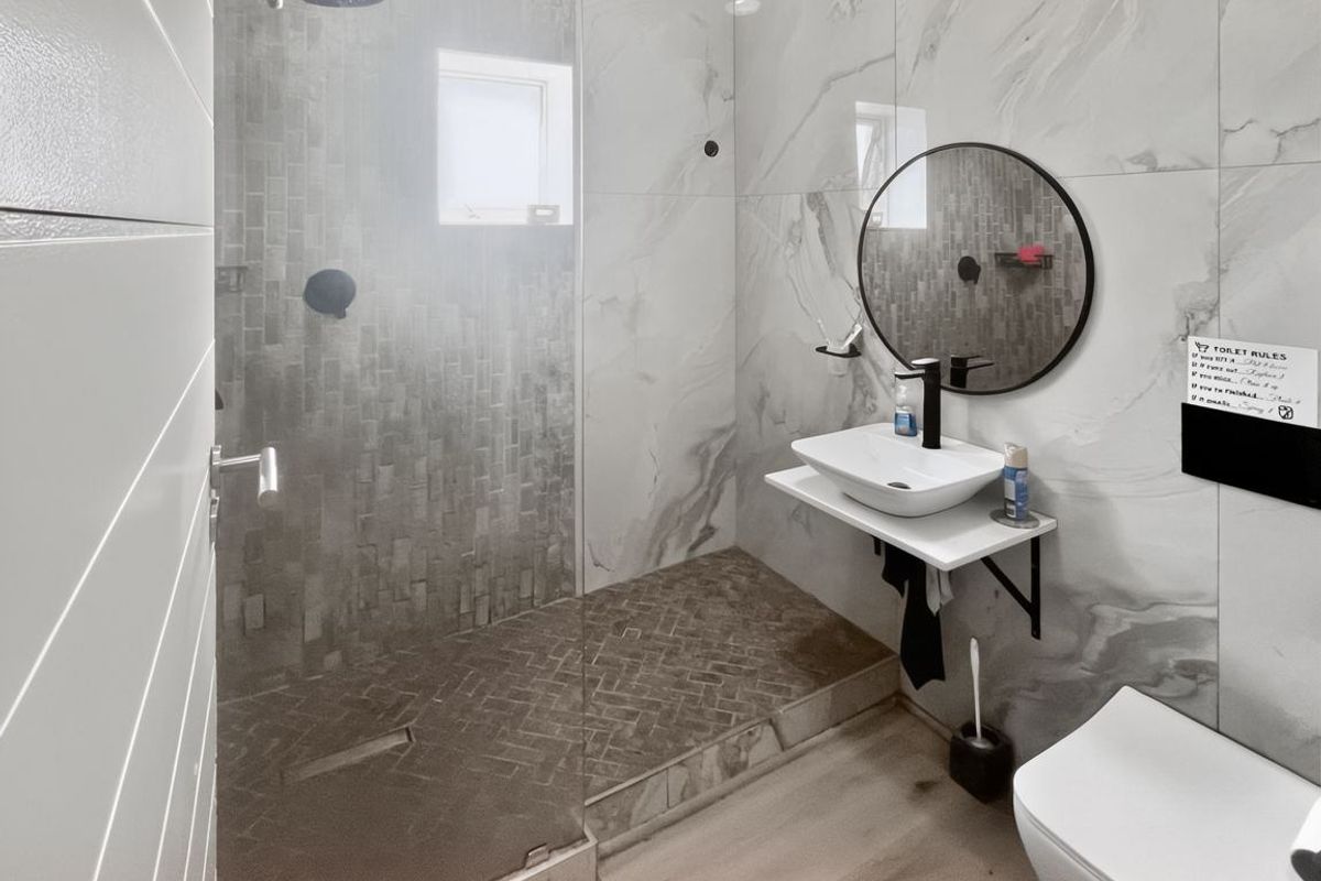 Modern bathroom featuring a walk-in shower with glass enclosure, marble-look wall tiles, vessel sink, and wall-mounted toilet.