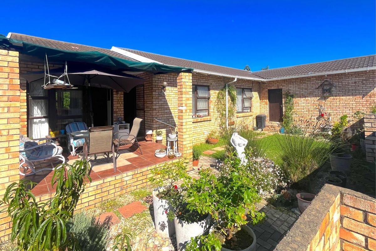 Rear view of the townhouse featuring a brick facade, a covered tiled patio area, and a landscaped garden with paved pathways.