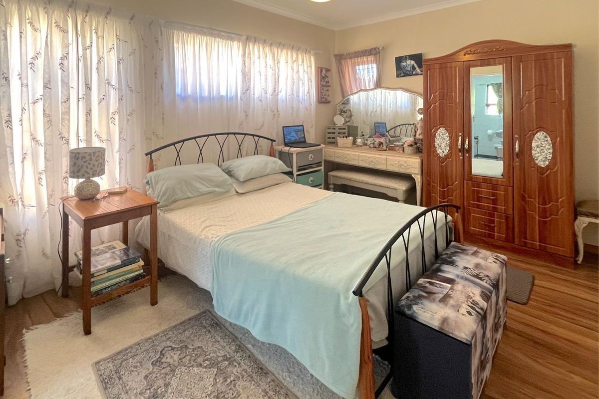 A functional bedroom featuring laminate flooring and neutral wall tones, offering a comfortable space with natural light through window treatments.