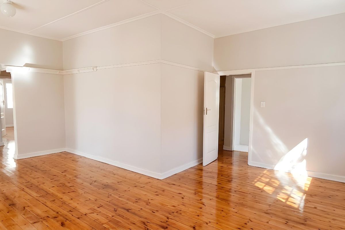 A bright and spacious living area featuring polished timber flooring, neutral wall tones, and classic picture rails.