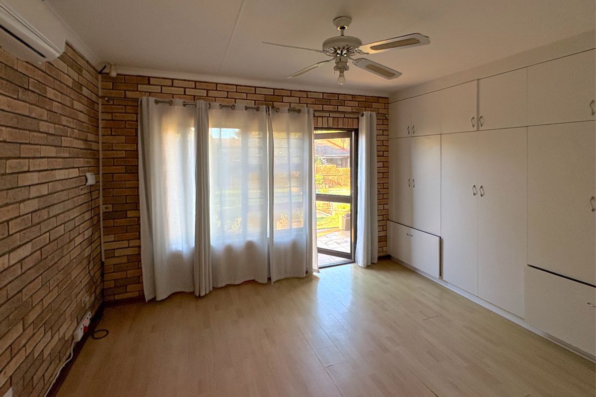 A bedroom featuring built-in cabinetry, laminate flooring, a ceiling fan, and direct access to the garden through a glass door.