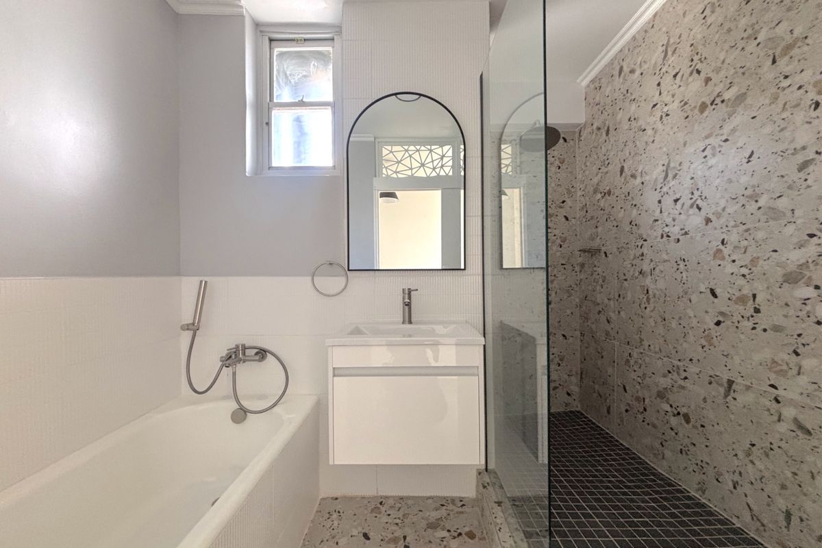 Modern bathroom featuring a floating vanity, a separate bathtub with handheld shower, and a spacious walk-in shower with terrazzo-style wall tiling.