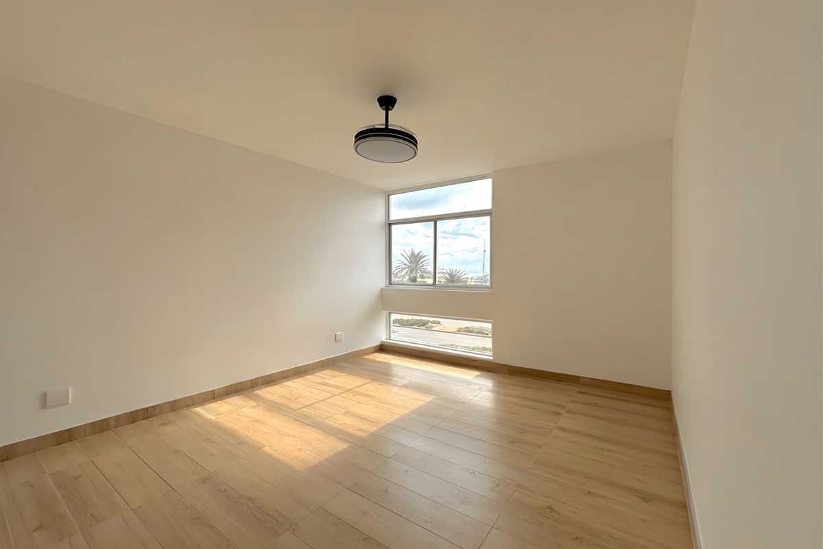 A bright, empty bedroom featuring modern wood-look tile flooring, neutral walls, and a ceiling fan, offering a clean and versatile living space.