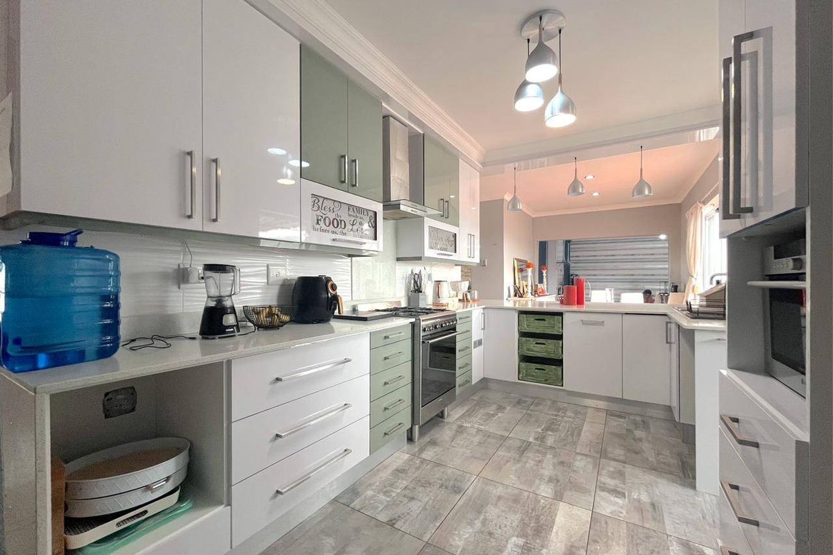 Modern kitchen featuring high-gloss cabinetry, stone countertops, stainless steel gas stove, extractor fan, and tiled flooring with integrated lighting.