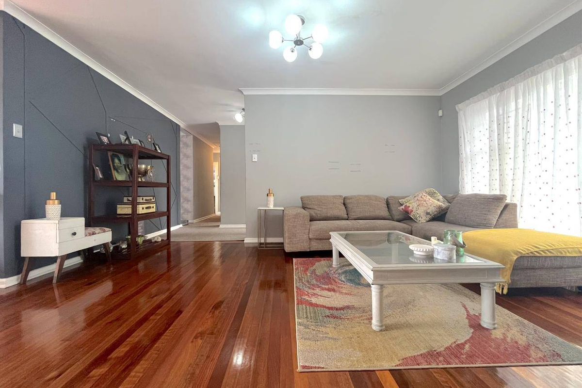 Spacious living room featuring polished timber flooring, a feature accent wall, and large windows allowing for natural light.
