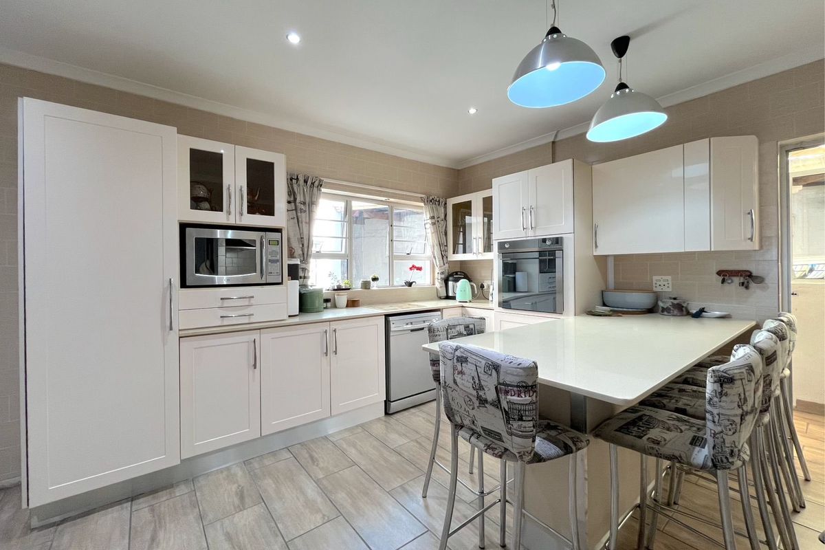 A well-maintained kitchen featuring white cabinetry, integrated oven and microwave, stone-look tiled flooring, and a central breakfast island with pendant lighting.