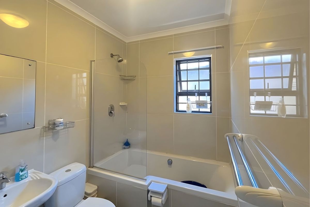 A clean and functional bathroom featuring a bathtub with a glass shower screen, wall-mounted shower head, toilet, and pedestal basin with tiled walls.