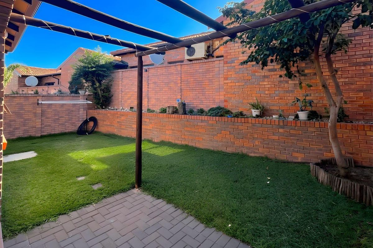 A private rear garden featuring a paved patio area, a timber pergola structure, and a brick retaining wall with established garden beds.