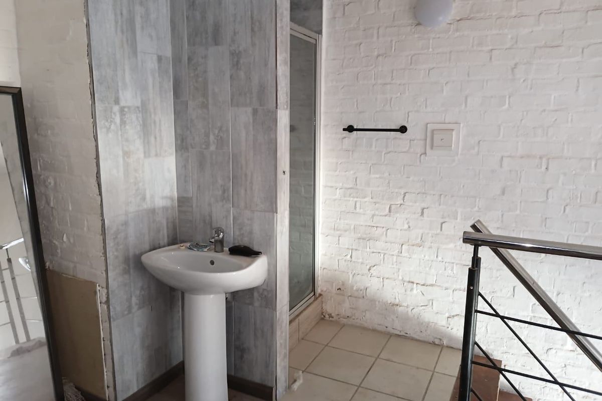 A bathroom area featuring a pedestal basin, a shower enclosure with glass door, and exposed brick wall detailing adjacent to a staircase.