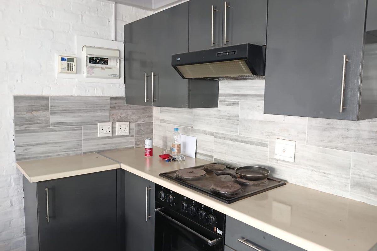A compact kitchen featuring dark grey cabinetry, light-toned countertops, wood-look tile backsplash, and a built-in oven with an extractor fan.