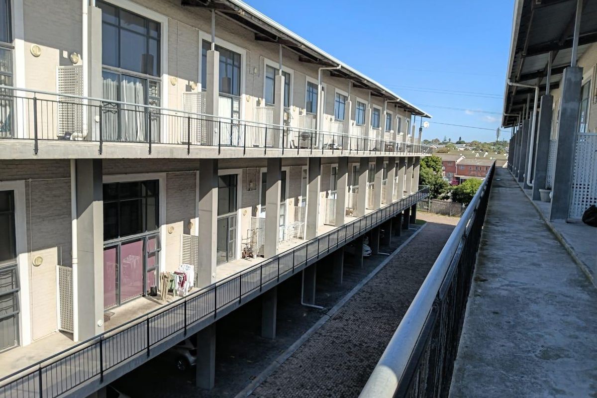 Exterior view of a multi-story apartment complex featuring concrete walkways, metal railings, and large glass sliding doors providing access to individual units.