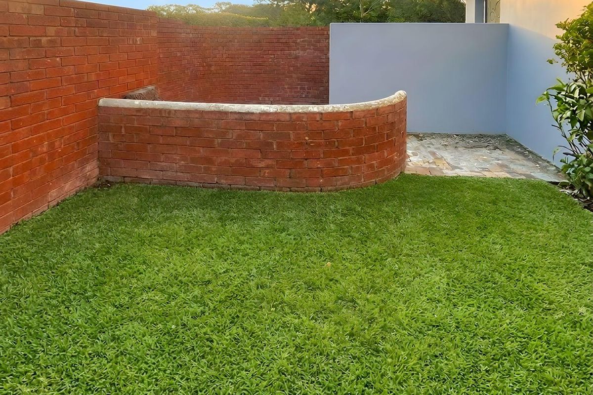 A private rear garden area featuring a curved brick retaining wall, a small paved section, and a well-maintained lawn.