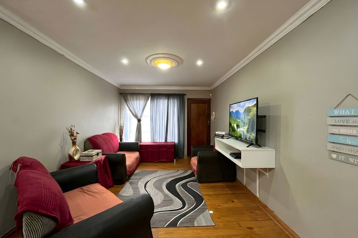 A cozy living room featuring polished timber flooring, recessed ceiling downlights, decorative ceiling rose, and a wall-mounted media console.