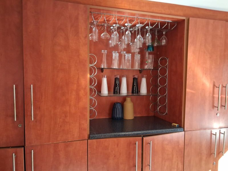Built-in wooden bar cabinetry featuring integrated glass shelving, stemware racks, and a dark stone-look countertop for beverage preparation.