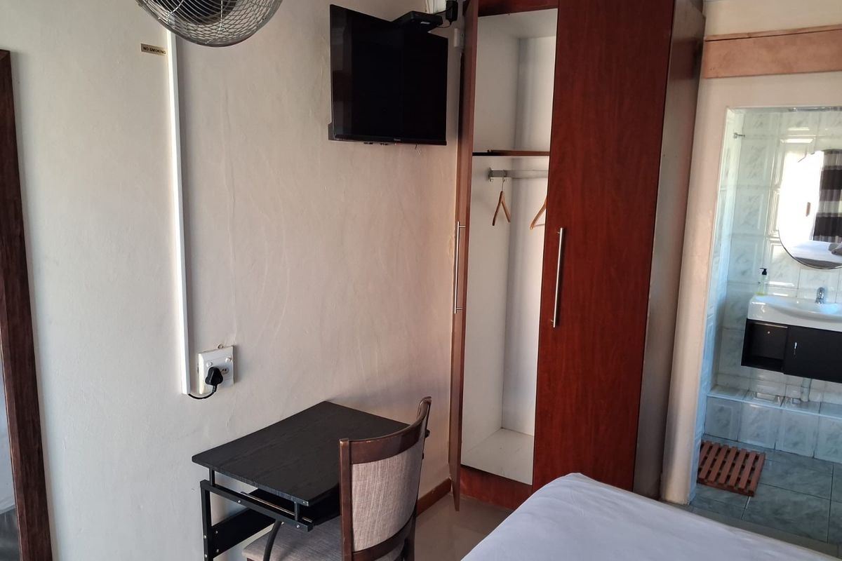 A compact bedroom featuring a built-in wooden wardrobe and an en-suite bathroom with a modern vanity unit.