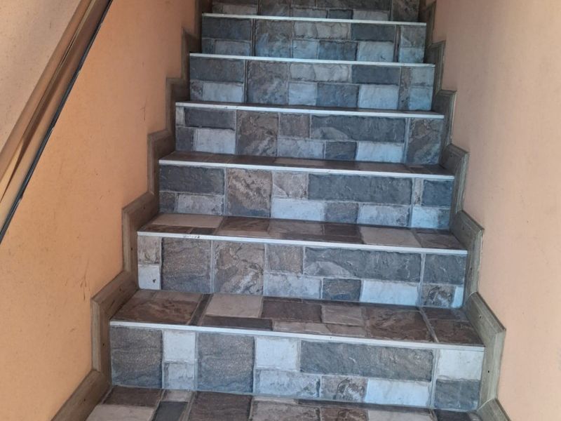 A staircase featuring stone-look tiled treads and risers with a simple handrail, providing access between levels in the commercial property.