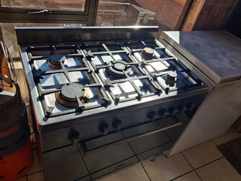 A stainless steel gas stove with five burners and an integrated oven, positioned in a kitchen area with tiled flooring.