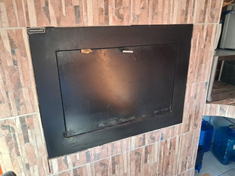A built-in Megamaster fireplace featuring a black metal door set within a tiled surround, suitable for indoor heating or entertainment areas.