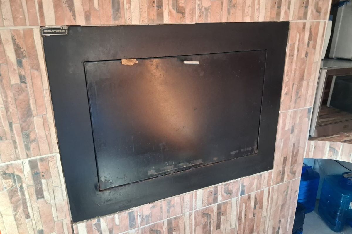 A built-in Megamaster fireplace featuring a black metal door set within a tiled surround, suitable for indoor heating or entertainment areas.