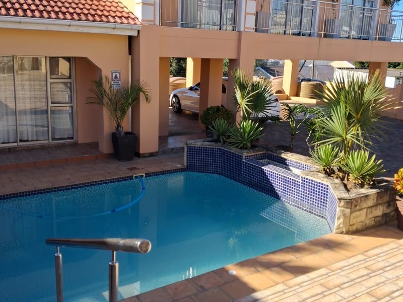 A well-maintained exterior view featuring a swimming pool with tiled surround, stainless steel pool railing, and a multi-level building with balconies.