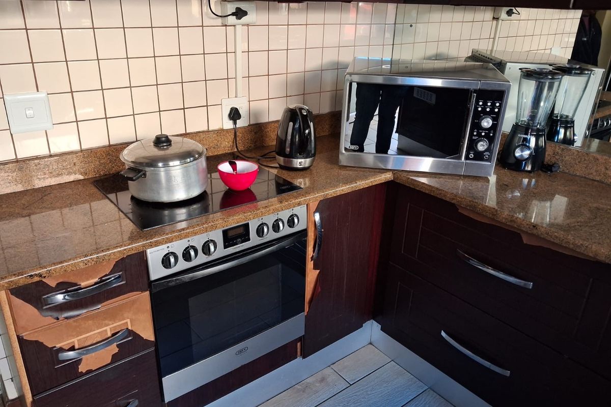 A kitchen workspace featuring dark cabinetry, granite countertops, a built-in oven, and a ceramic hob with tiled splashback.