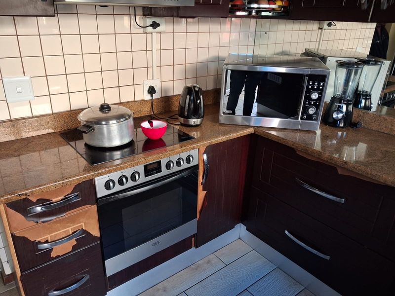 A kitchen workspace featuring dark cabinetry, granite countertops, a built-in oven, and a ceramic hob with tiled splashback.