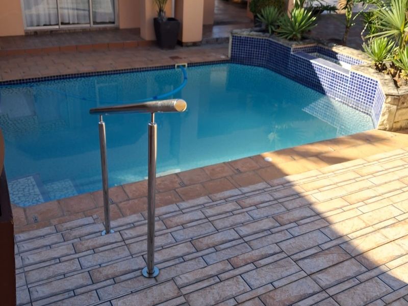 Outdoor pool area featuring tiled decking, a stainless steel safety handrail, and a raised tiled pool surround with integrated landscaping.