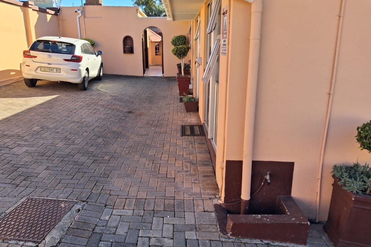 Exterior view of a commercial property featuring paved driveway, brick boundary walls, and access to a rear courtyard area.