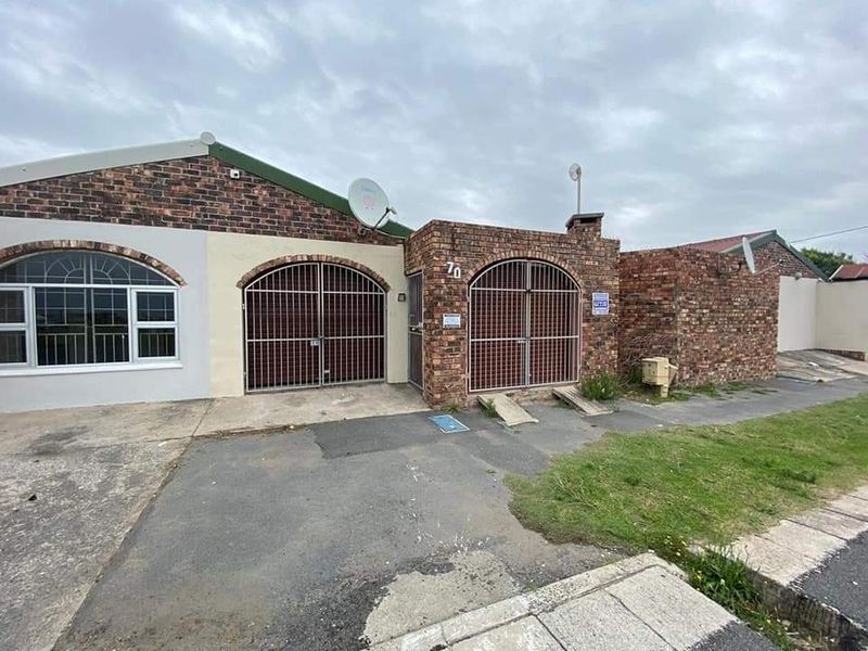 Front elevation of a single-story brick house featuring arched security gates, a paved driveway, and a satellite dish.