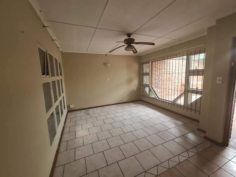 A spacious, empty living area featuring tiled flooring, a ceiling fan, and large windows with security bars.