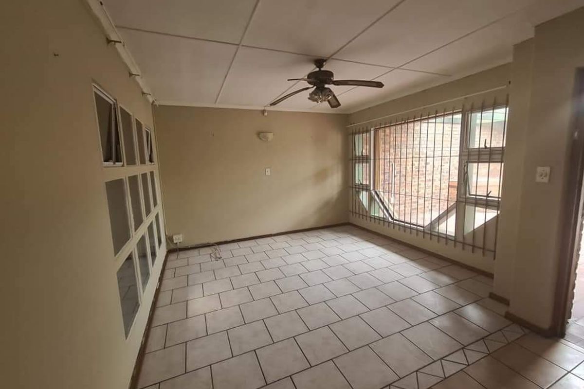 A spacious, empty living area featuring tiled flooring, a ceiling fan, and large windows with security bars.