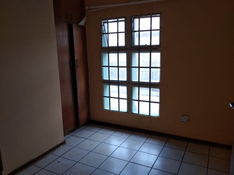 A bedroom featuring tiled flooring, built-in wooden cupboards, and a window with security bars.