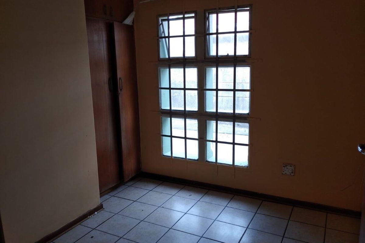 A bedroom featuring tiled flooring, built-in wooden cupboards, and a window with security bars.