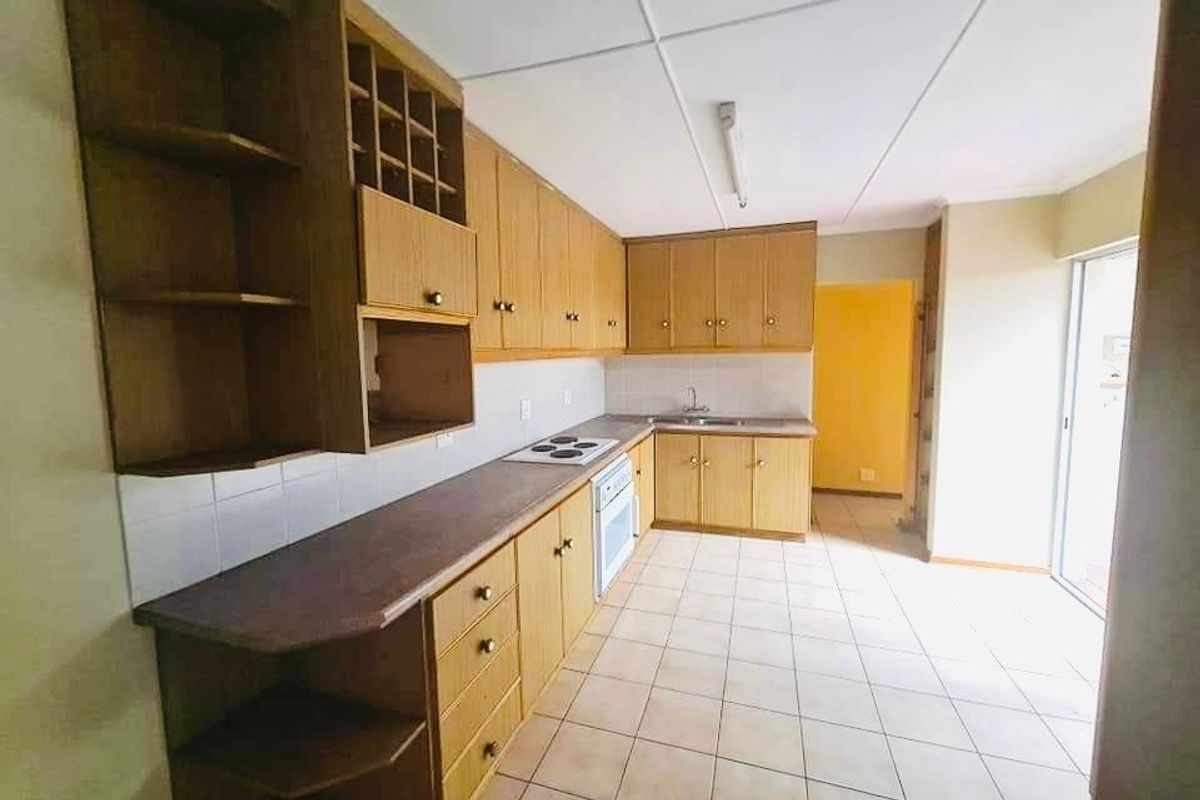 A functional kitchen featuring wood-finish cabinetry, integrated stove and oven, tiled flooring, and direct access to an outdoor area.
