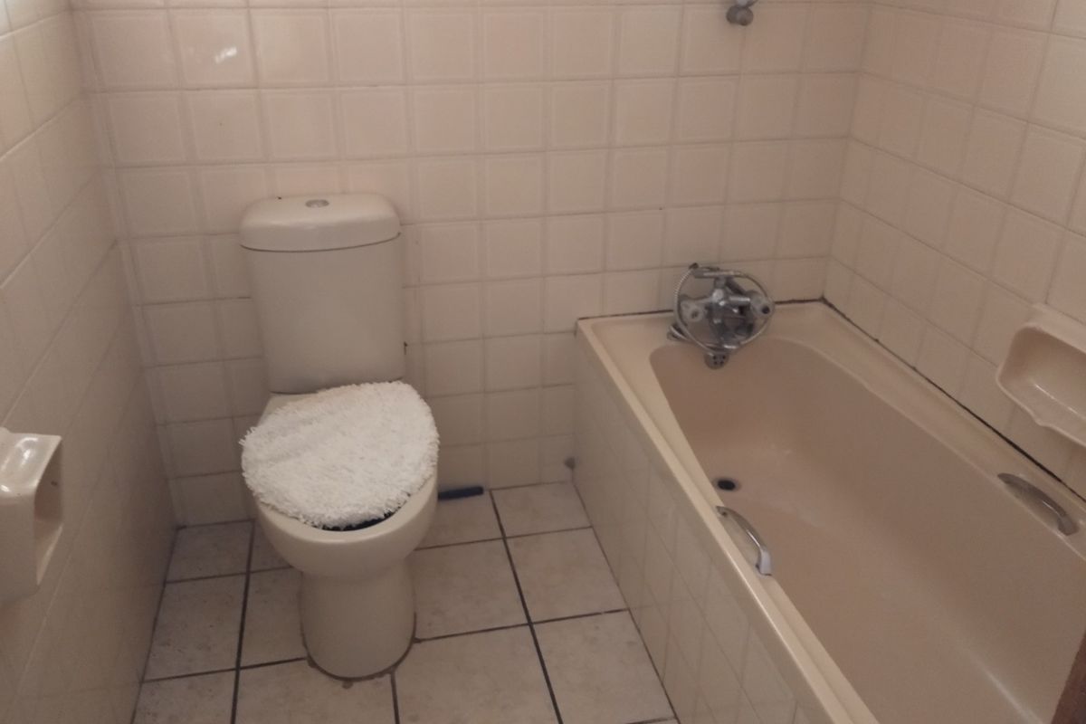 A compact bathroom featuring a standard bathtub with shower mixer and a toilet, finished with neutral wall and floor tiles.