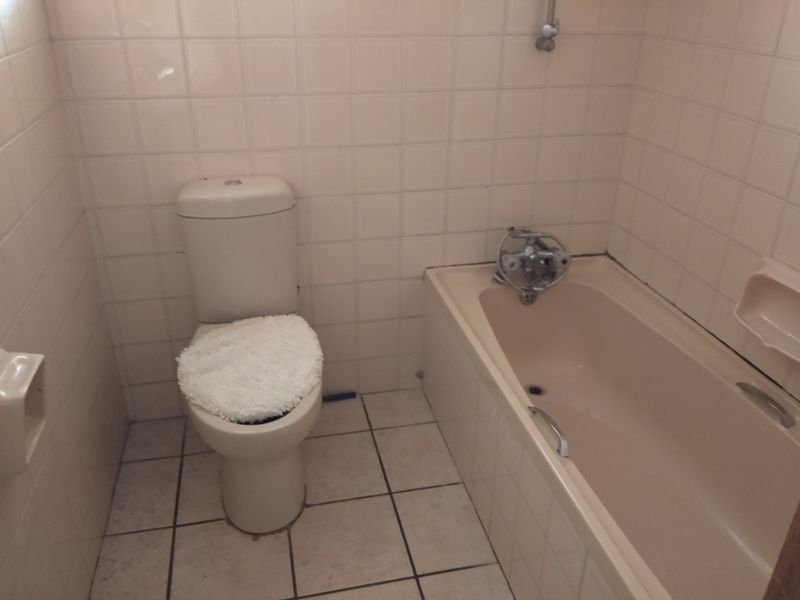 A compact bathroom featuring a standard bathtub with shower mixer and a toilet, finished with neutral wall and floor tiles.