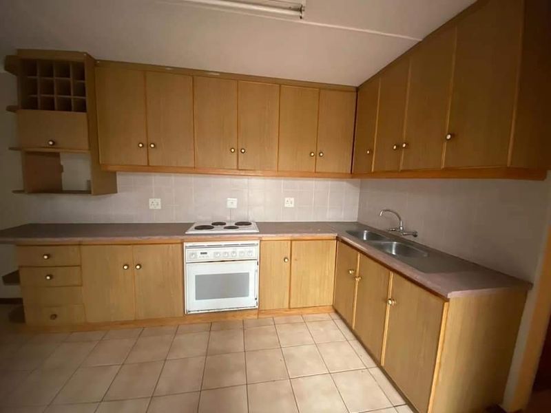 A functional kitchen featuring wood-finish cabinetry, integrated oven and hob, double stainless steel sink, and tiled flooring.