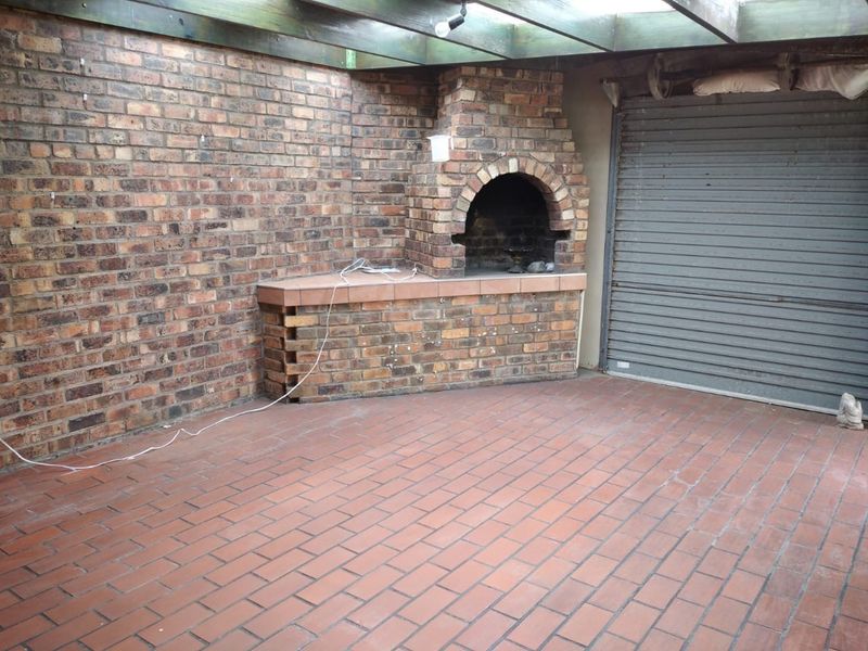 Outdoor patio area featuring a built-in brick fireplace, paved flooring, and a covered pergola structure with a roller shutter door.