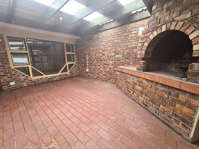 Covered patio area featuring a built-in brick fireplace, exposed brick walls, and paved flooring under a translucent roof structure.
