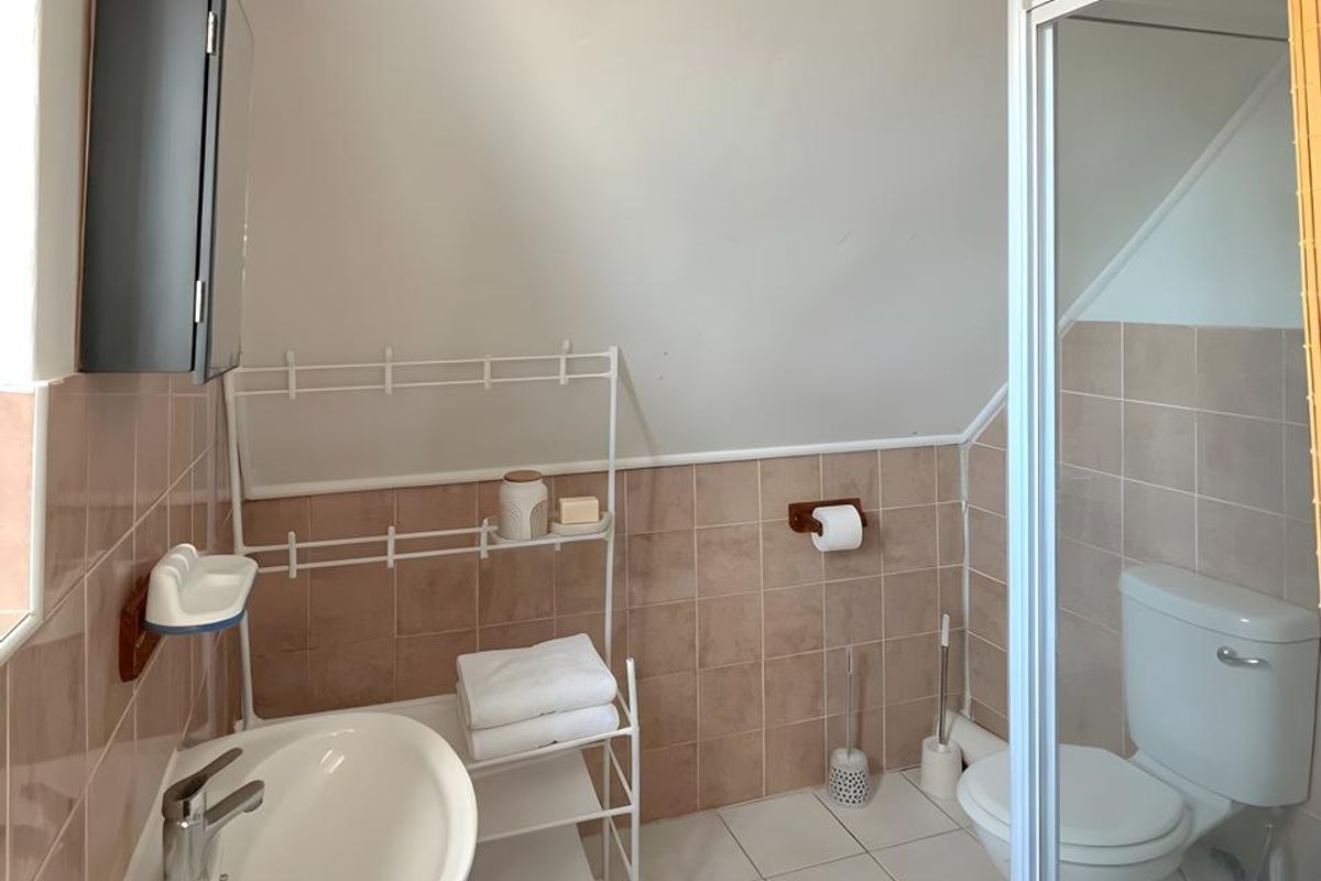A compact bathroom featuring a pedestal sink, a shower enclosure with a glass door, and a toilet, finished with neutral wall and floor tiles.