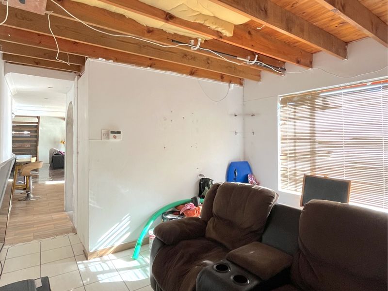 A living area featuring exposed timber ceiling beams and tiled flooring, currently requiring ceiling completion and electrical finishing.