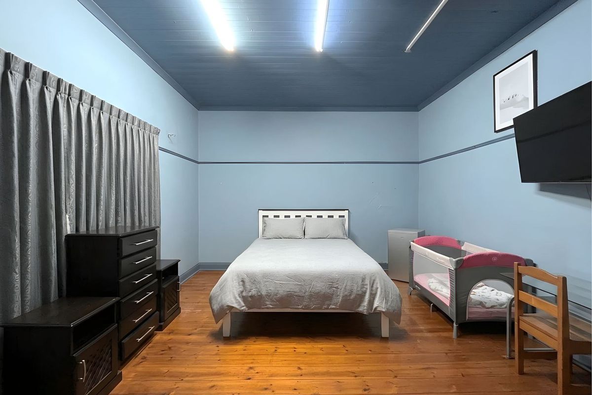 Spacious bedroom featuring polished timber flooring, high ceilings with exposed beams, and a neutral blue color palette.