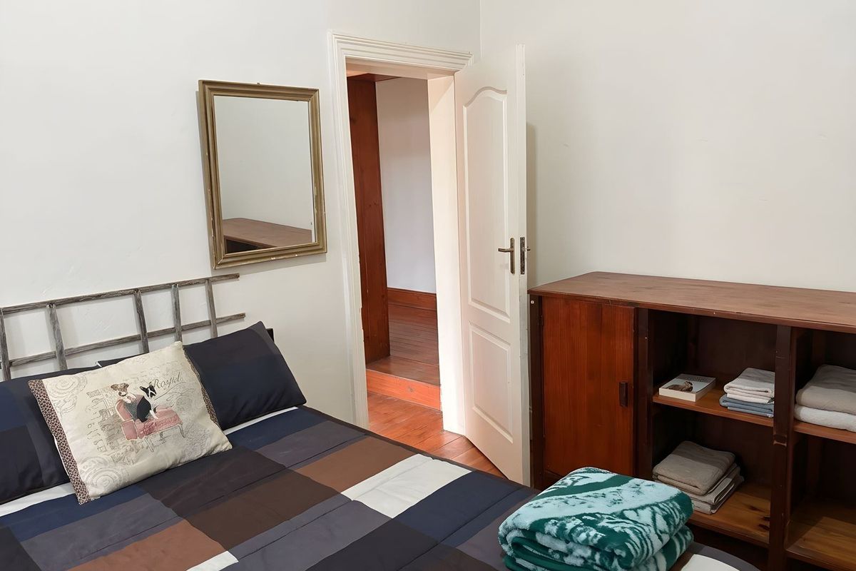 A bedroom featuring white walls, wooden flooring visible in the adjacent hallway, and a standard interior door.