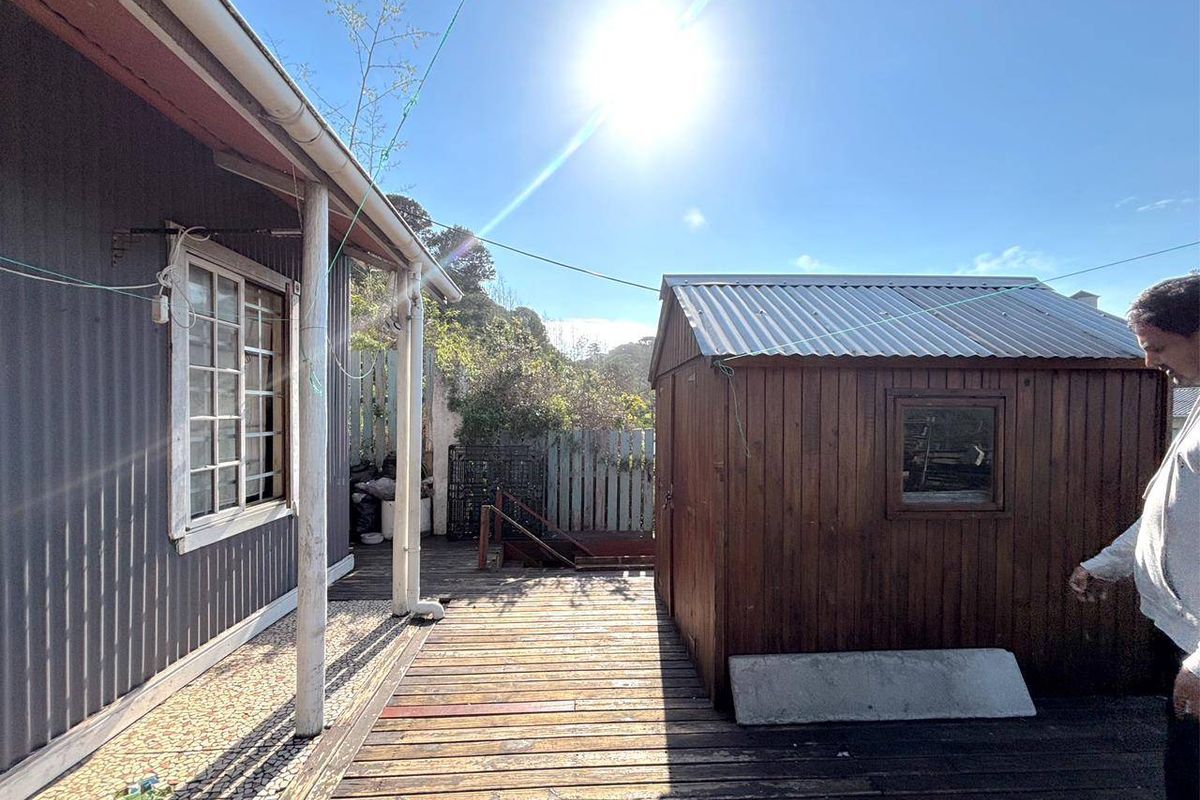 Rear exterior view featuring a timber deck, a detached wooden storage shed, and corrugated metal wall cladding.