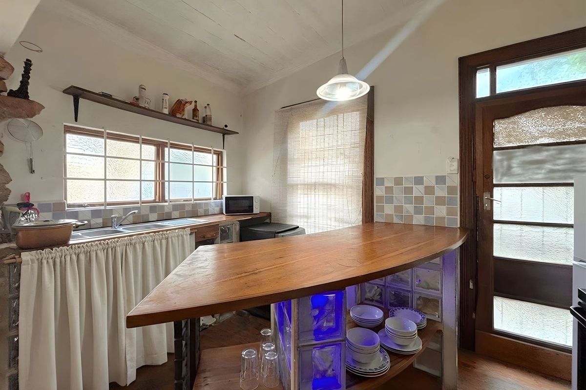 A rustic kitchen featuring a custom wooden breakfast bar, glass block base, double sink, and timber door leading to the exterior.