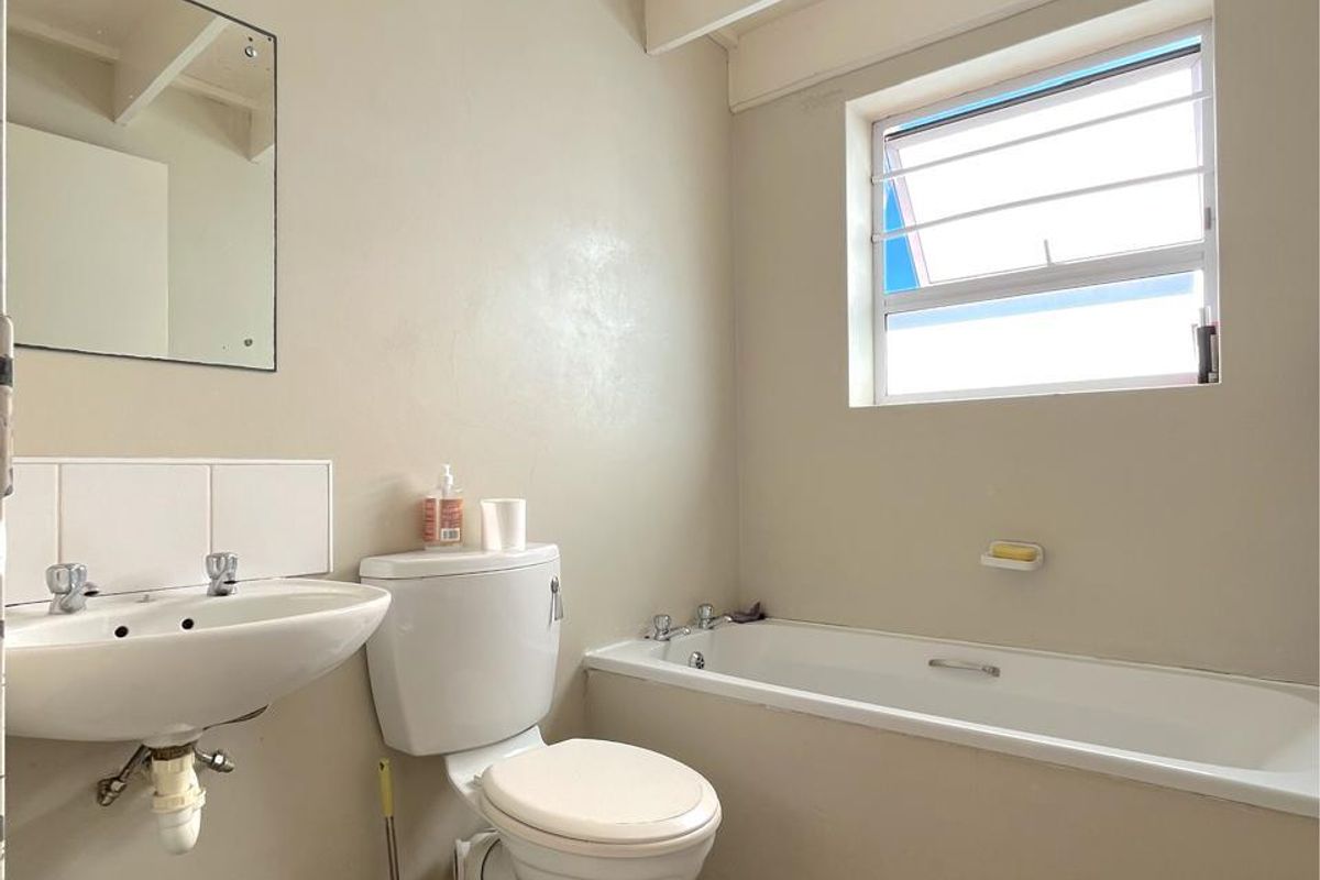 A functional bathroom featuring a standard bathtub, pedestal sink, and toilet, with exposed ceiling beams and tiled flooring.