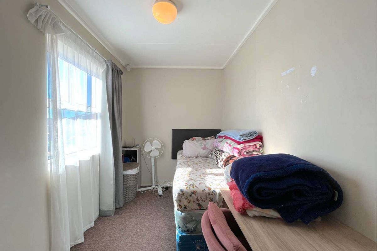 A compact bedroom featuring carpeted flooring, a large window for natural light, and a central ceiling light fixture.