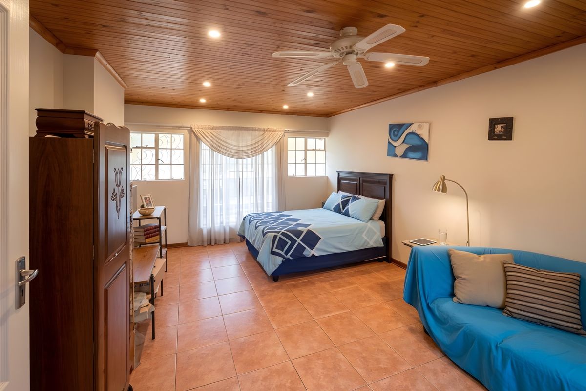 Spacious bedroom featuring a warm timber-paneled ceiling, tiled flooring, recessed lighting, and a ceiling fan, offering a comfortable and functional living space.