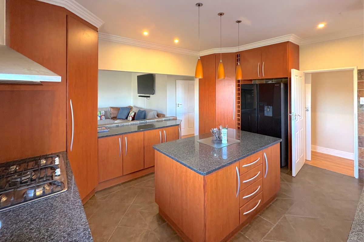 A well-appointed kitchen featuring warm wood cabinetry, granite countertops, a central island, and integrated gas hob, offering a functional and inviting cooking space.