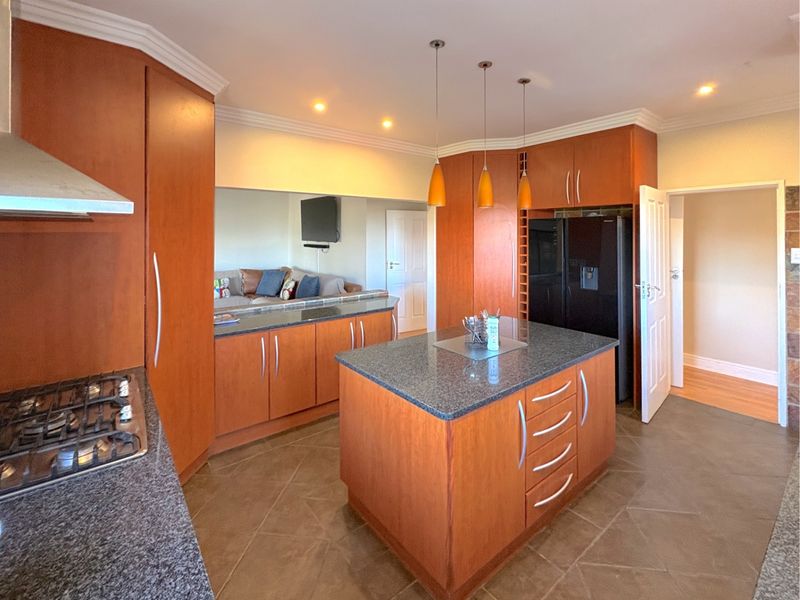 A well-appointed kitchen featuring warm wood cabinetry, granite countertops, a central island, and integrated gas hob, offering a functional and inviting cooking space.